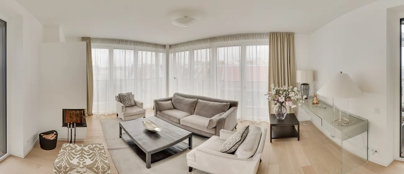 Helles, eingerichtetes Wohnzimmer mit Sofa, Kamin und Fensterfront, dahinter offene Küche mit Essplatz und Dachterrasse, als 360-Grad-Panorama